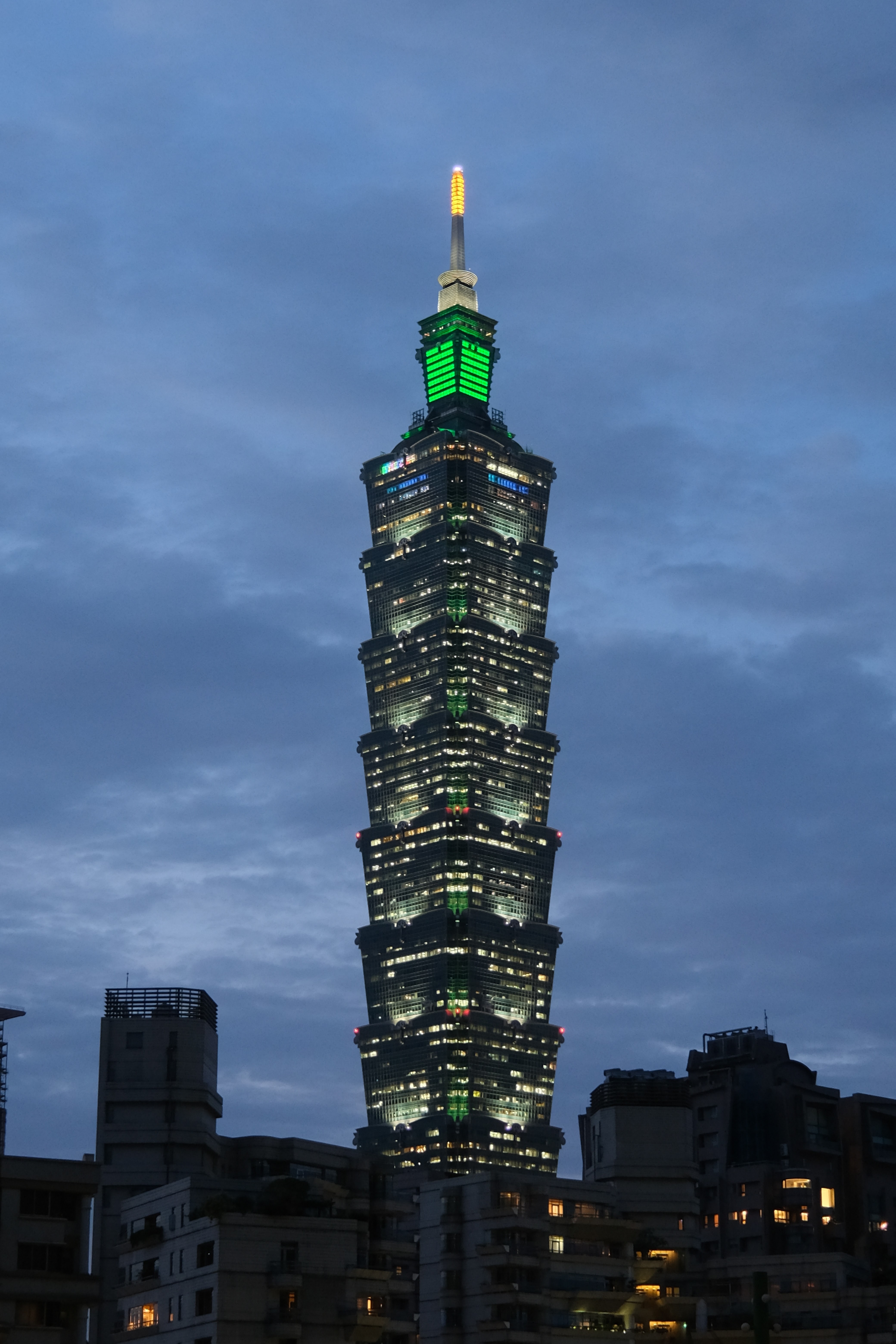 台北101大樓夜景，建築物燈光亮起，背景是傍晚的天空。