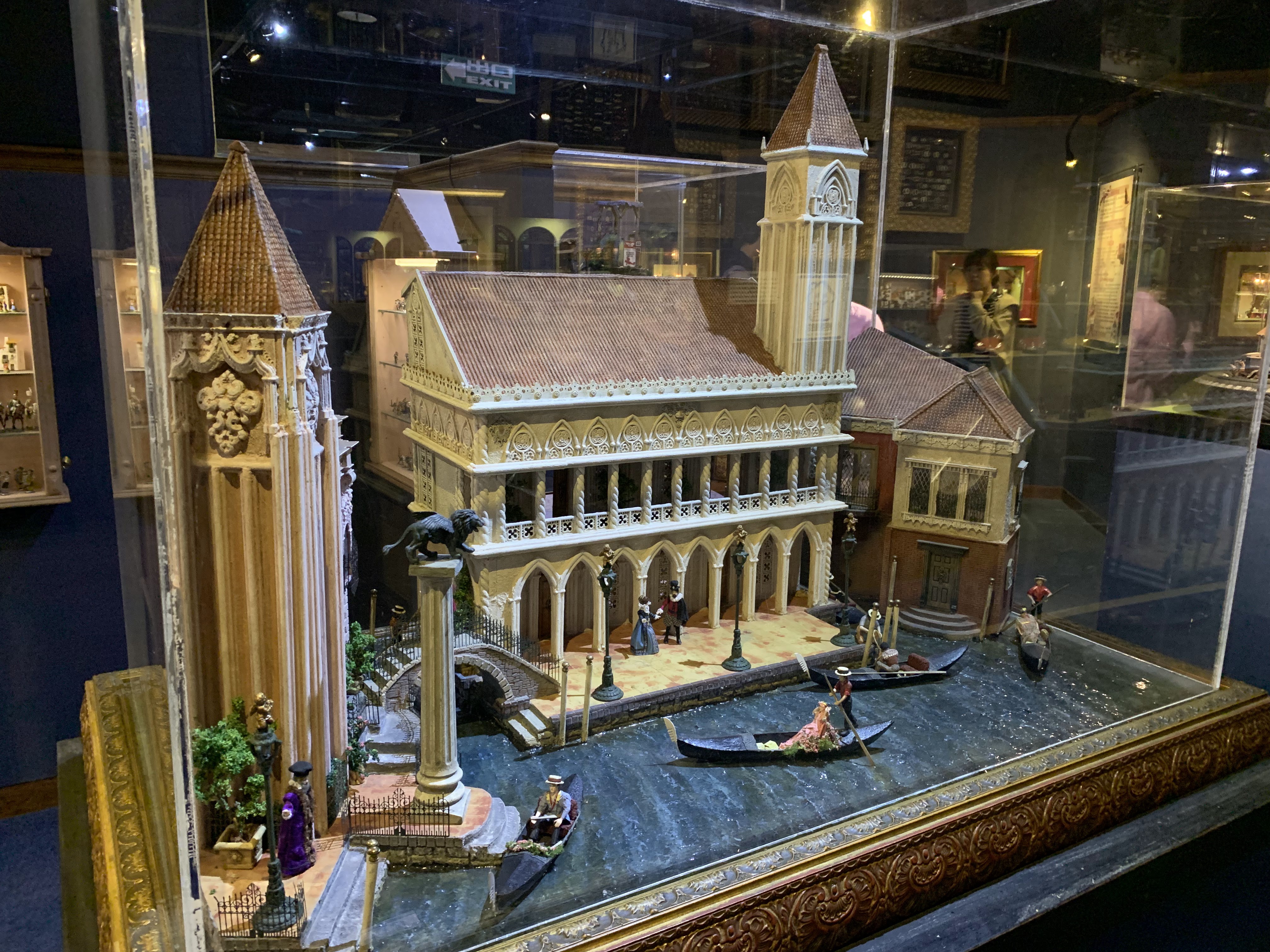 這張圖片展示了一個精緻的迷你威尼斯建築與運河模型，有精美的宮殿、鐘樓、小橋以及穿梭的貢多拉和人物，栩栩如生地還原了當地風情。圖片無明顯浮水印。