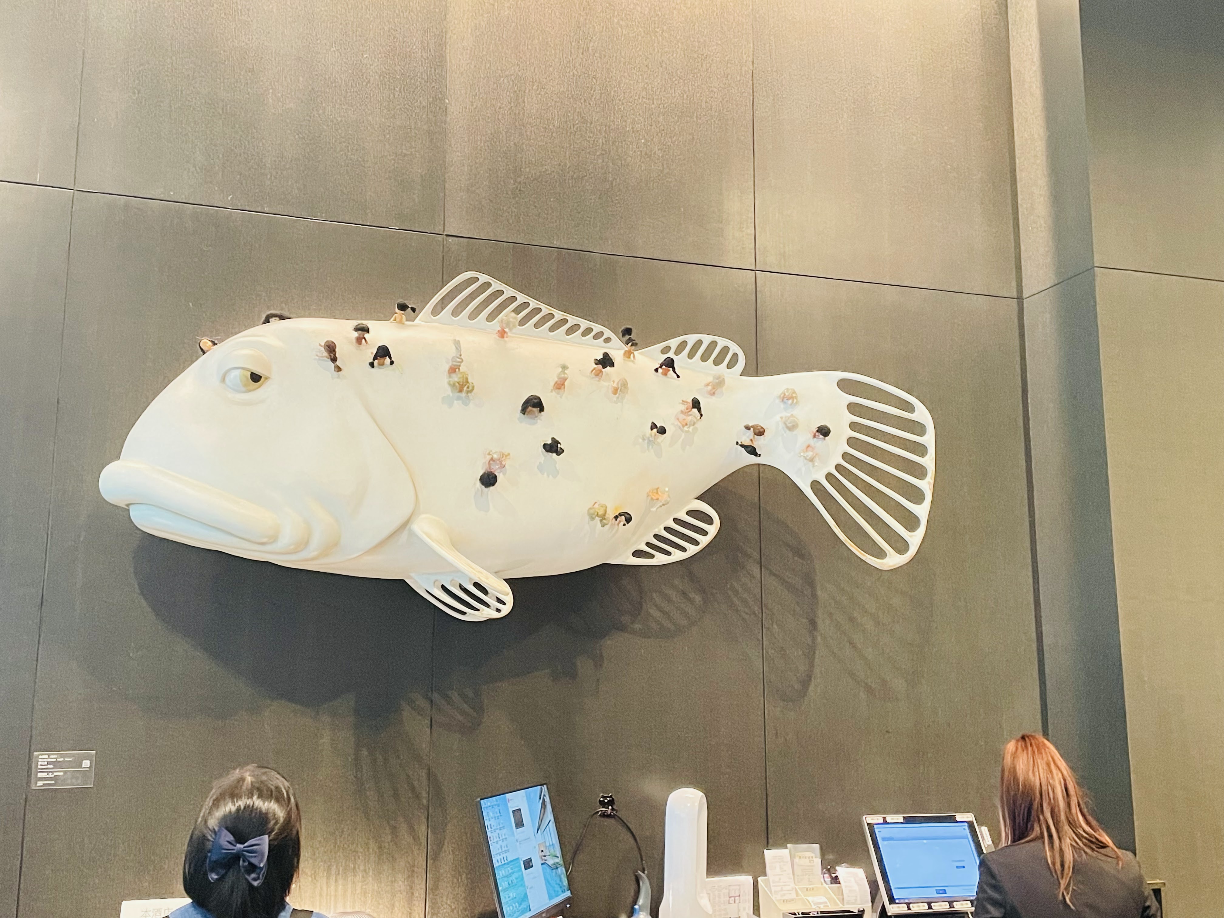 這張圖片主要展示了一隻巨大的白色魚形雕塑，魚身上有許多小人物模型，場景類似於大廳或接待處。圖片中沒有明顯的浮水印。