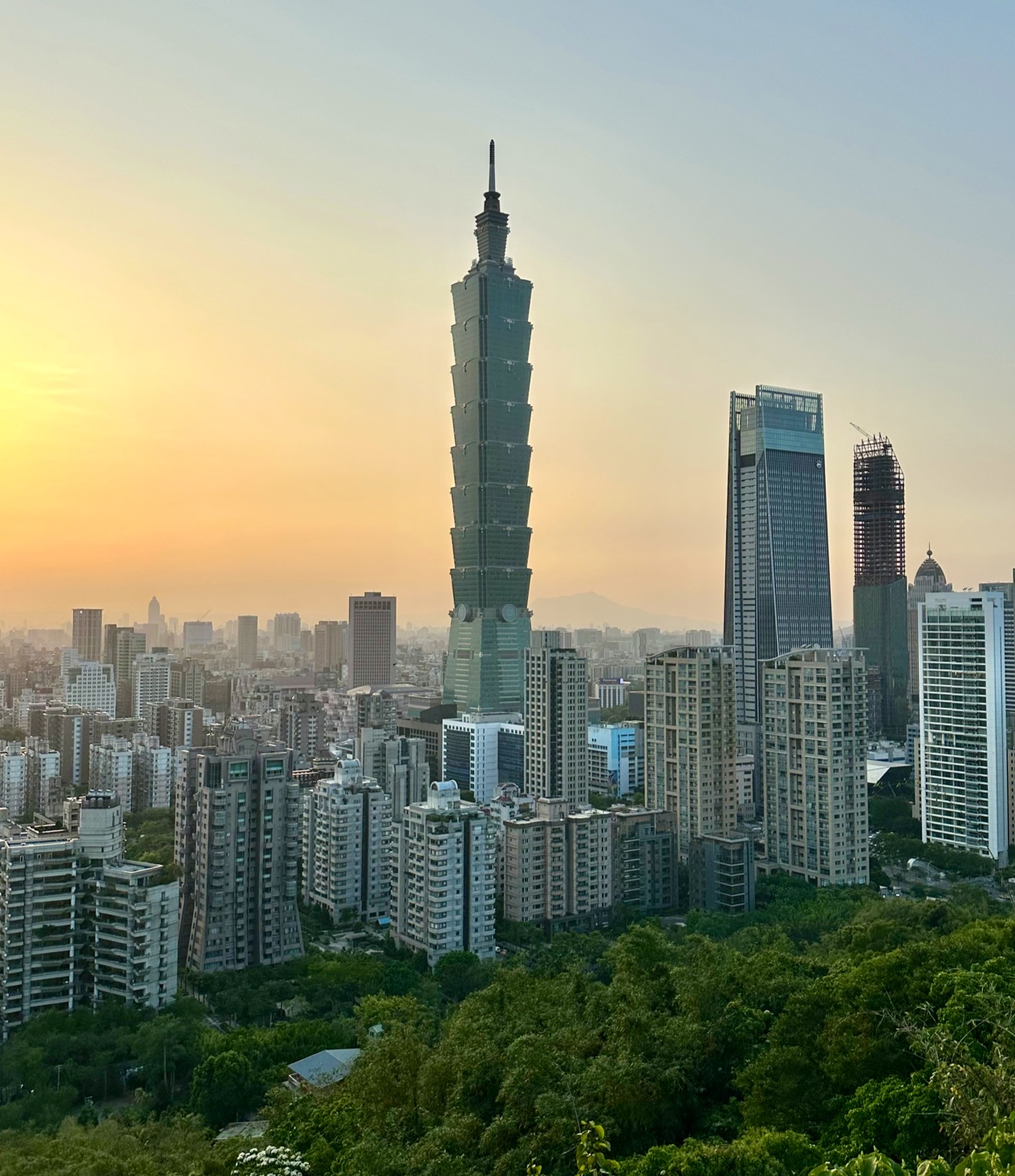 台北市天際線，中央有台北101大樓，背景為夕陽。