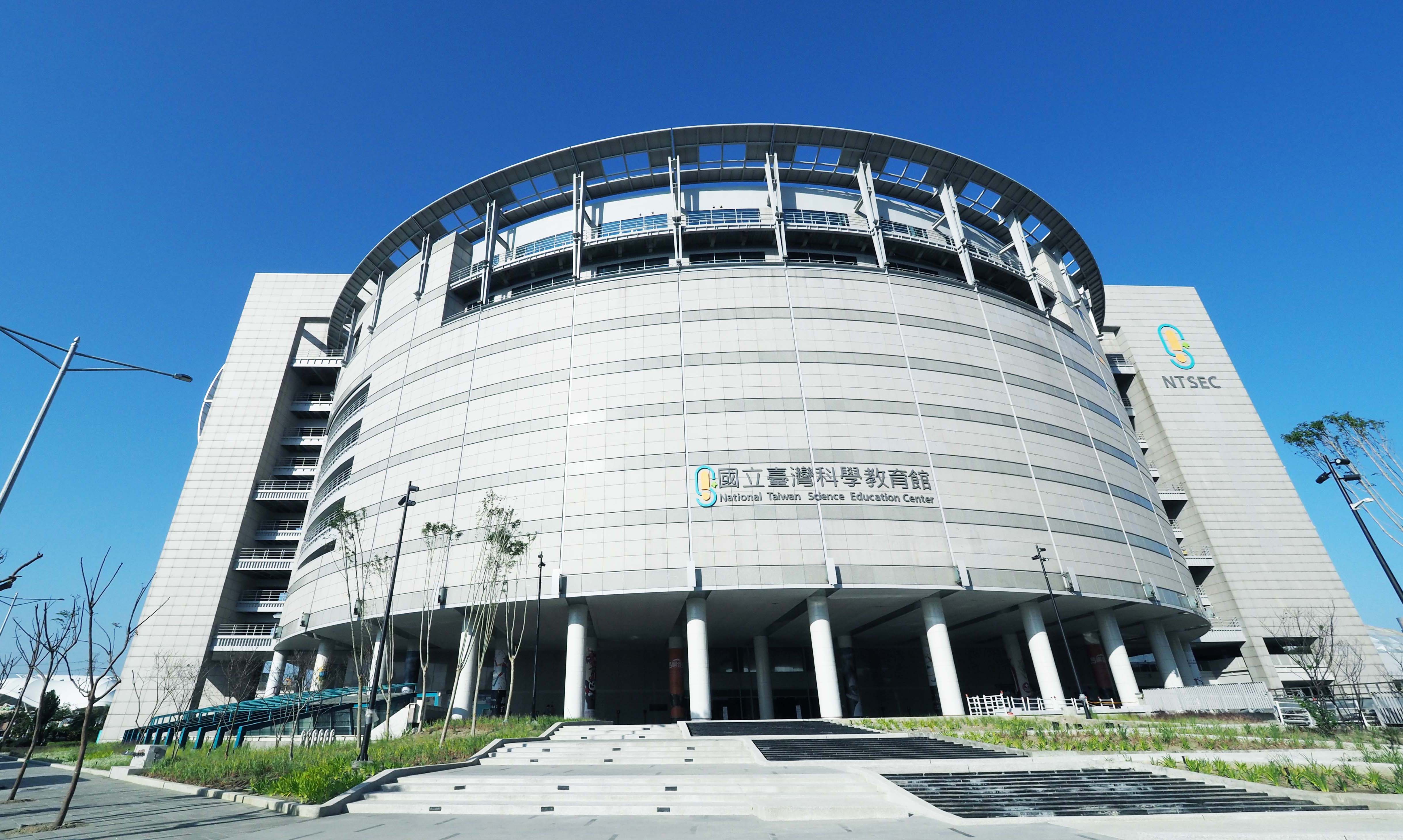 這張圖片主要顯示國立臺灣科學教育館建築物外觀，為一座現代化圓弧形設計的大型建築，前方有階梯和植栽，天空蔚藍，沒有浮水印。