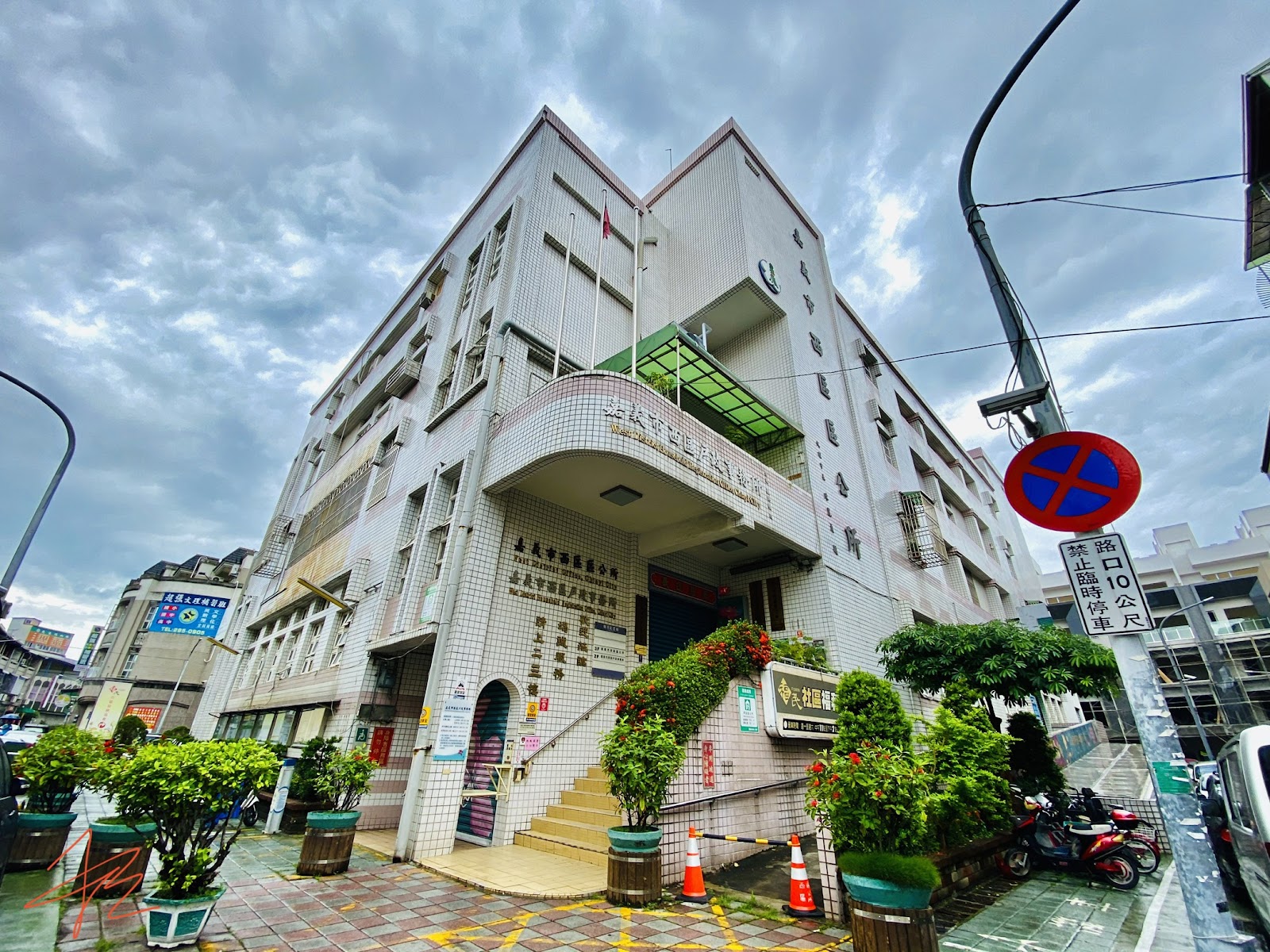 嘉義市西區公所白天外觀,白色磁磚五層樓建築,門口有盆栽與機車停放