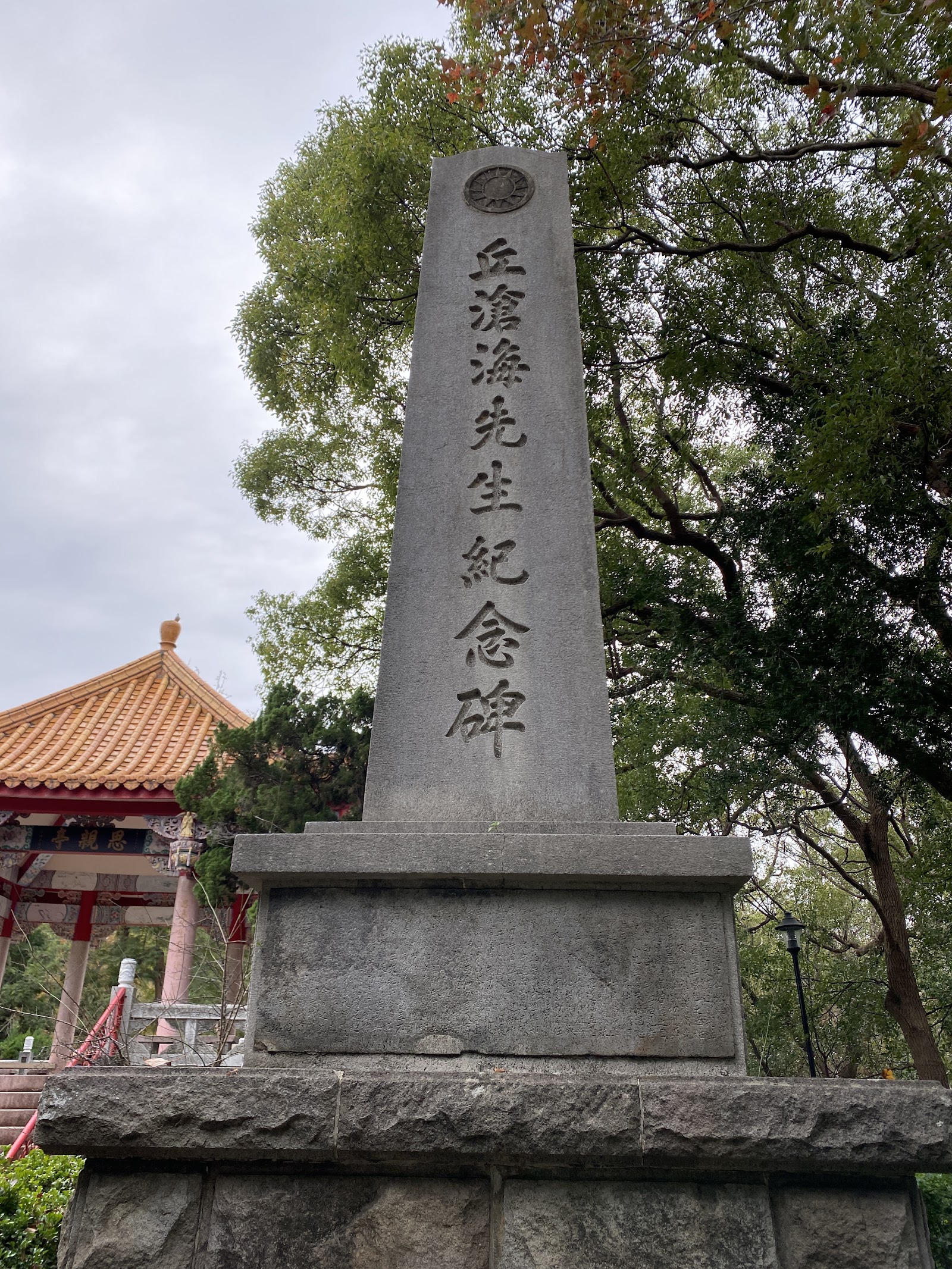 丘滄海先生紀念碑方形石碑，背景可見忠烈祠屋頂