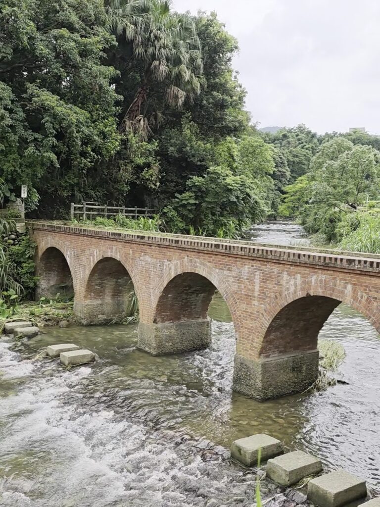 紅磚五拱橋橫跨溪流，兩岸綠樹扶疏，古樸韻味十足