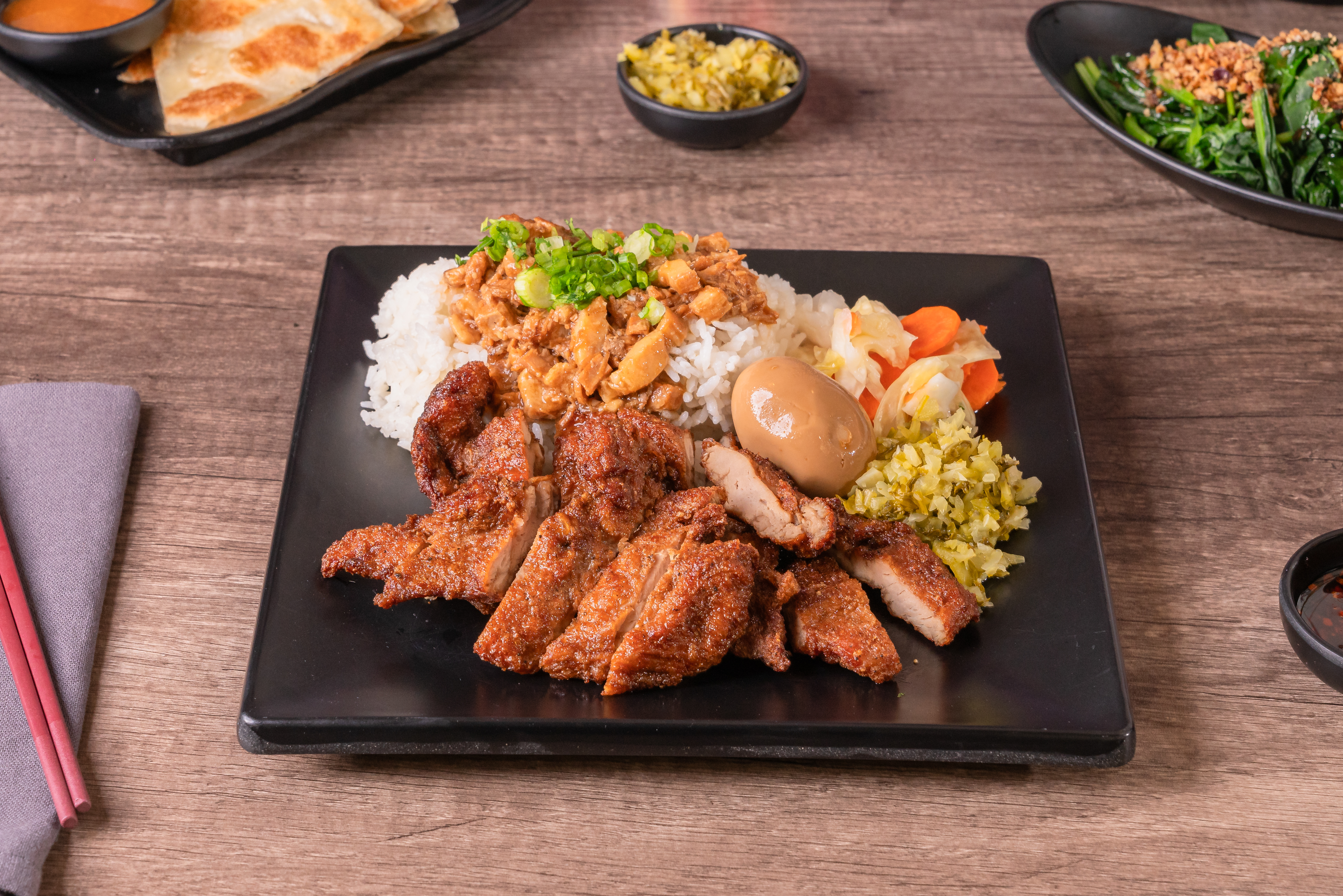 這張圖片主要是一份美味的台式便當,有白飯、滷肉、香煎雞腿、滷蛋、醃製蔬菜與配菜,旁邊還有蔬菜和餅等配菜。圖片無明顯浮水印。