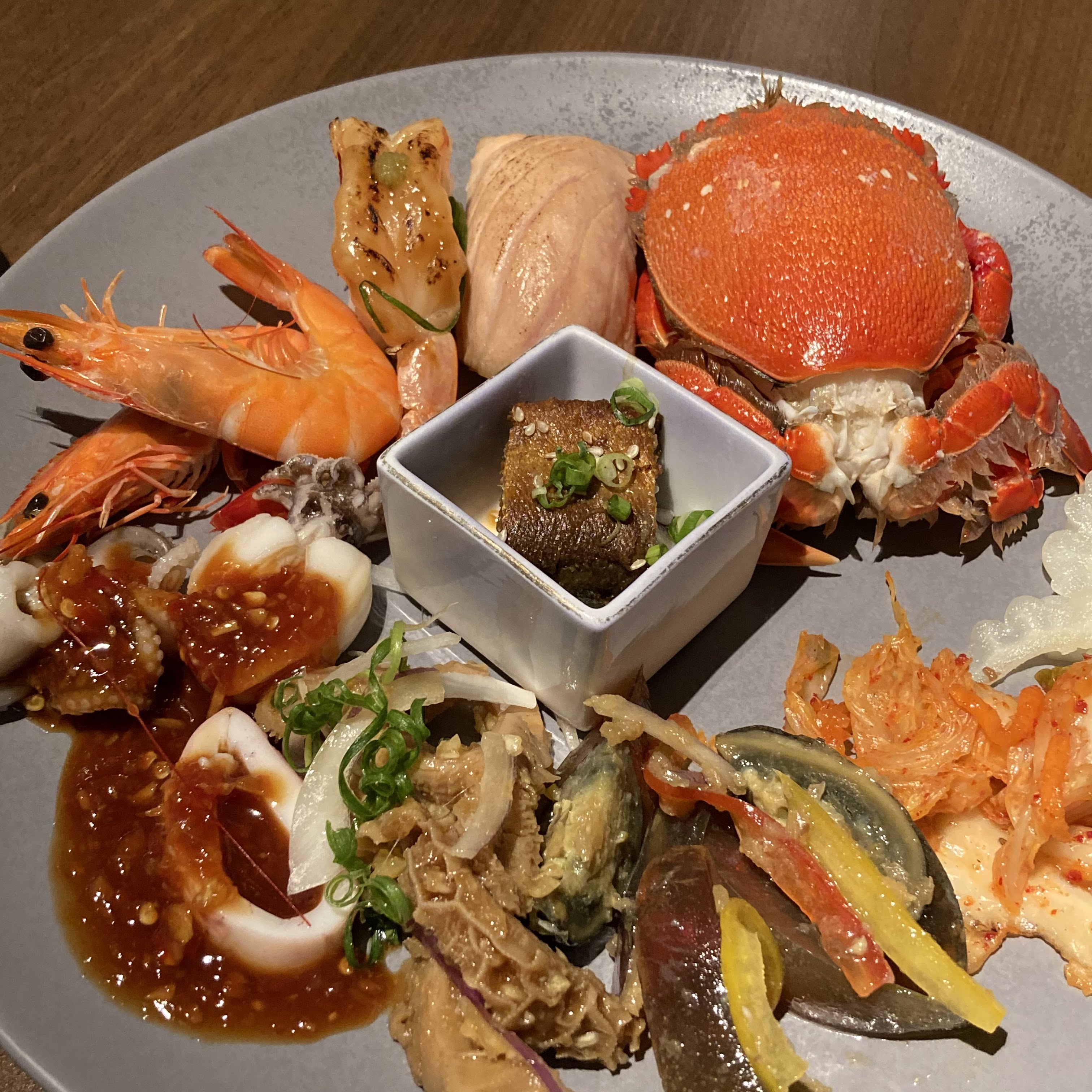 這張圖片展示了一盤中日混合風味的冷盤料理,包括螃蟹、蝦、炙燒壽司、醬燒花枝、皮蛋、牛肚、泡菜等豐富多樣的海鮮及配菜。畫面色彩鮮明,沒有浮水印。