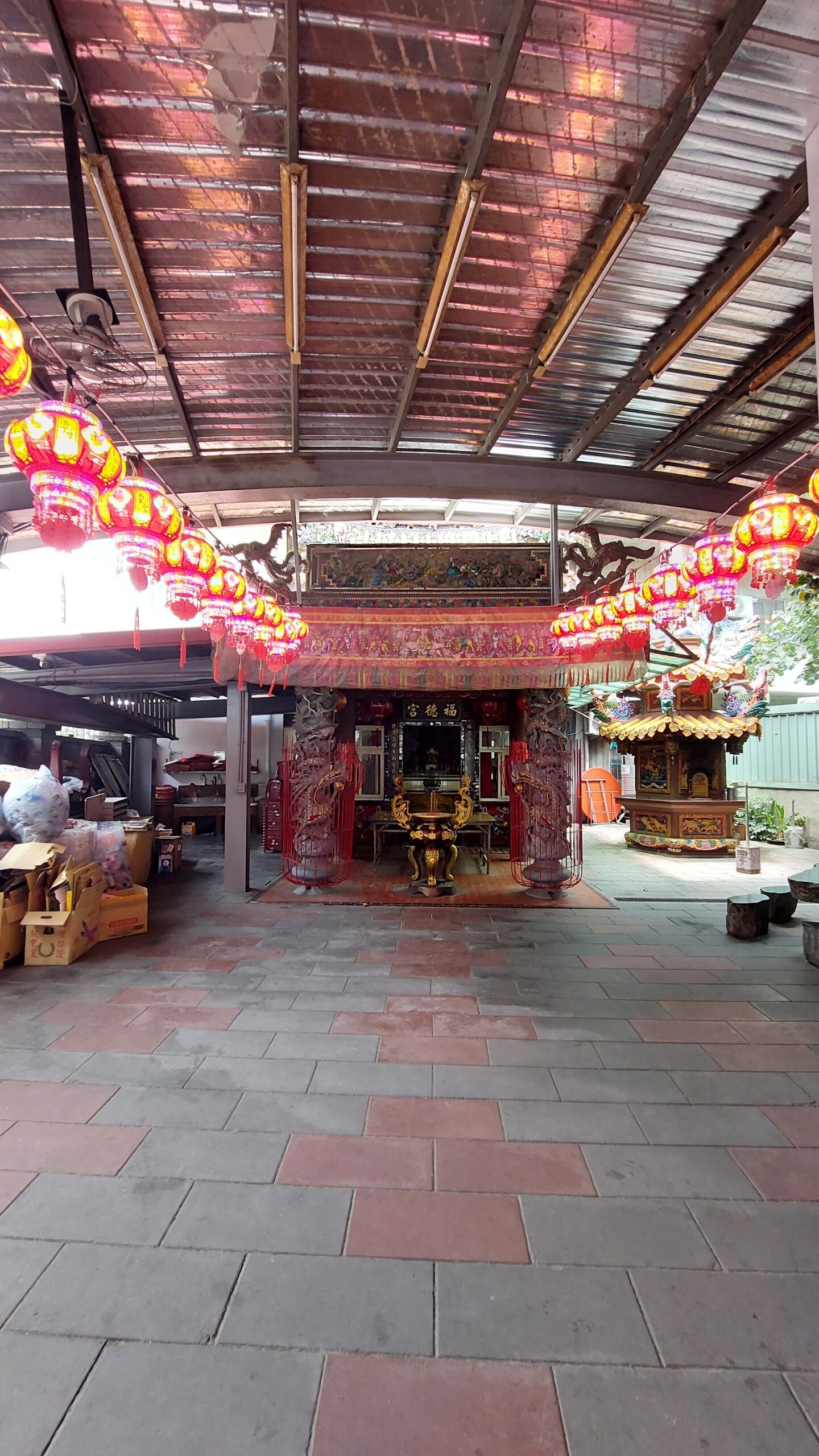 八里福德宮廟埕走廊紅燈籠成排懸掛,底端神龕與鐵皮屋頂