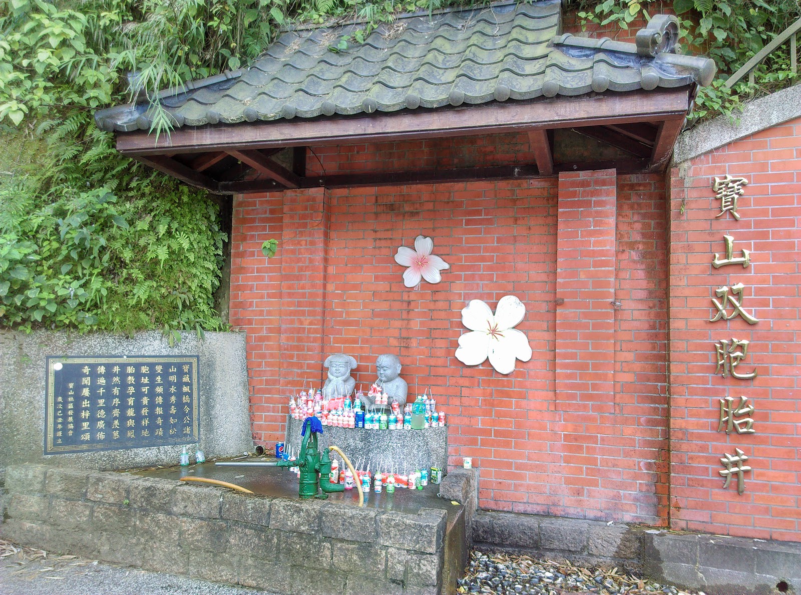 寶山雙胞胎井紅磚牆面與雙胞胎公仔，井口擺滿信眾供品