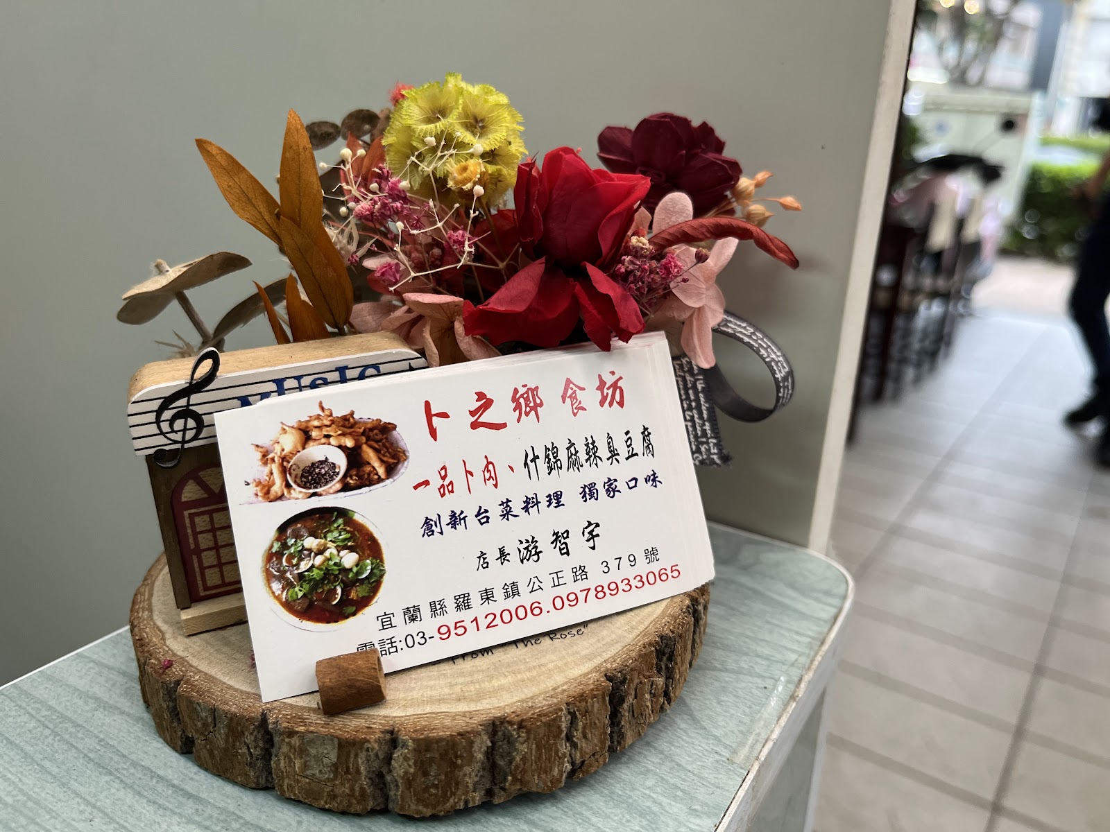 卜之鄉食坊店門口擺放的乾燥花束名片座,寫著店名與主打菜色