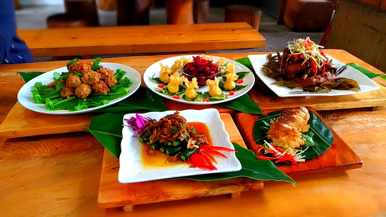 達基力部落屋木桌上擺放五道部落風味菜餚，含炸物、涼拌野菜、月桃葉烤肉