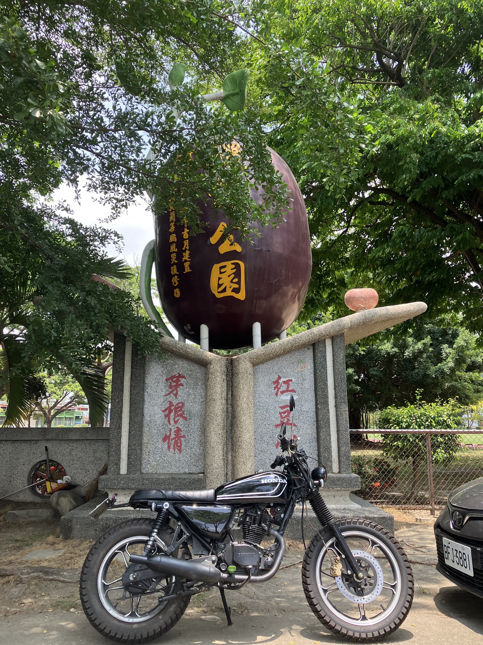 翁園大紅豆巨型紫紅色紅豆意象裝置藝術，立於石座上，周圍綠樹環繞