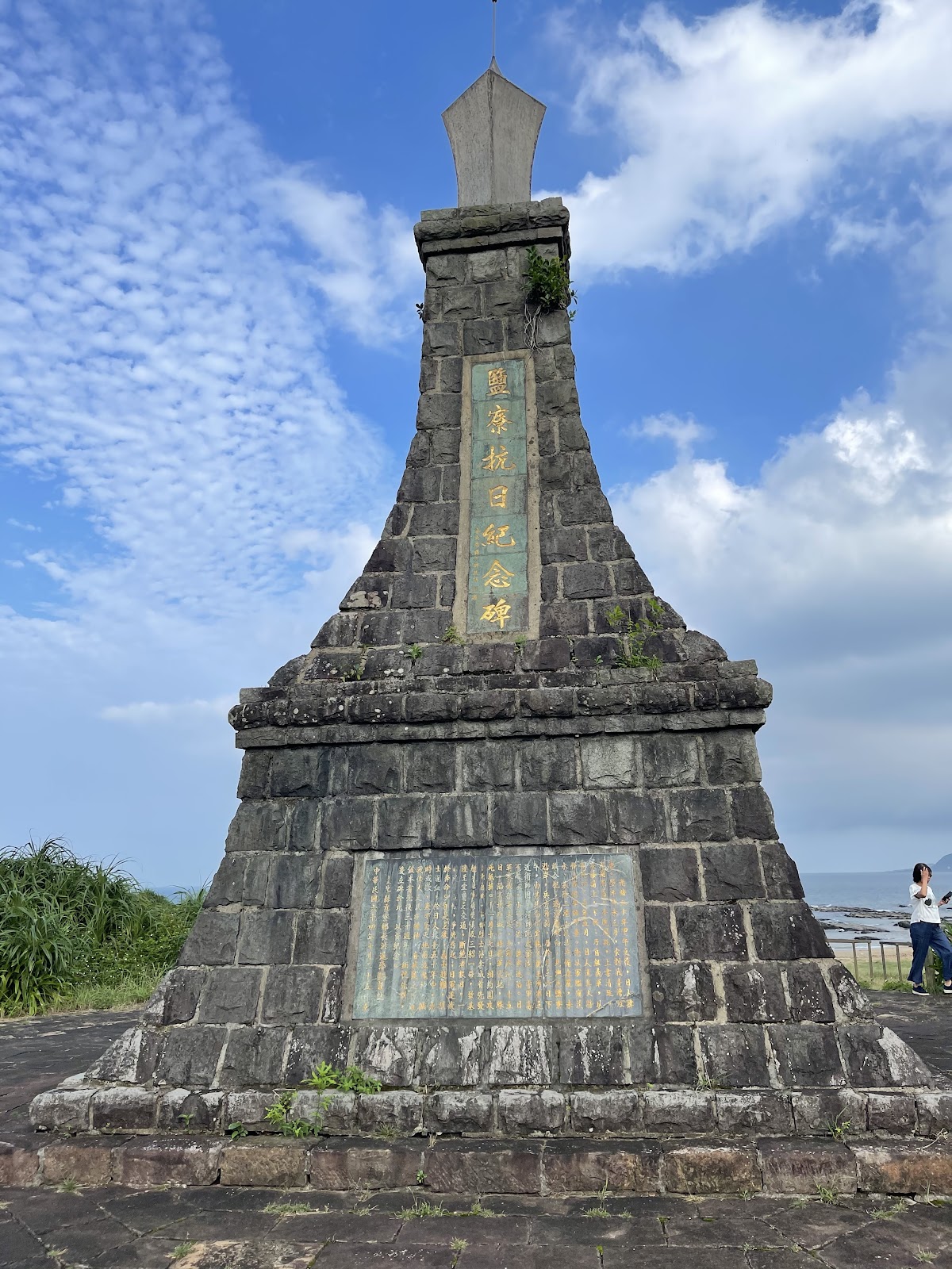 鹽寮抗日紀念碑灰白石砌尖塔造型全景，藍天背景
