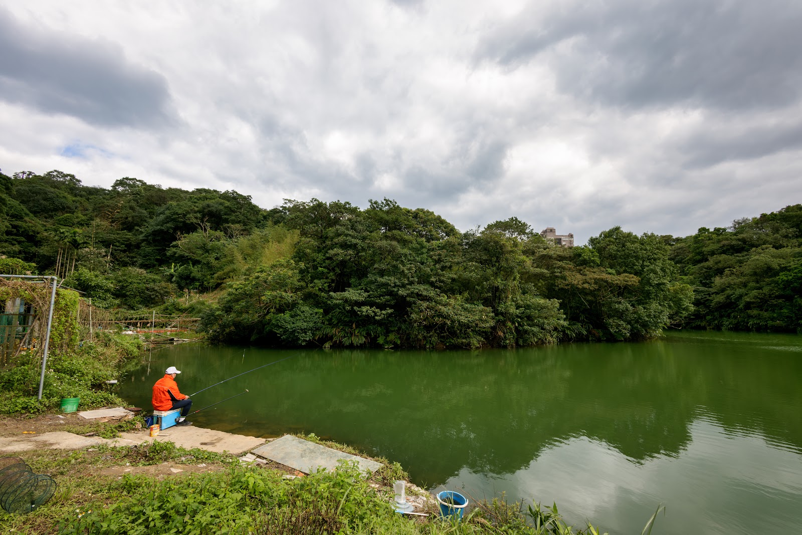 一位釣客坐在茵夢湖畔垂釣，湖水呈現墨綠色｜基隆信義區茵夢湖