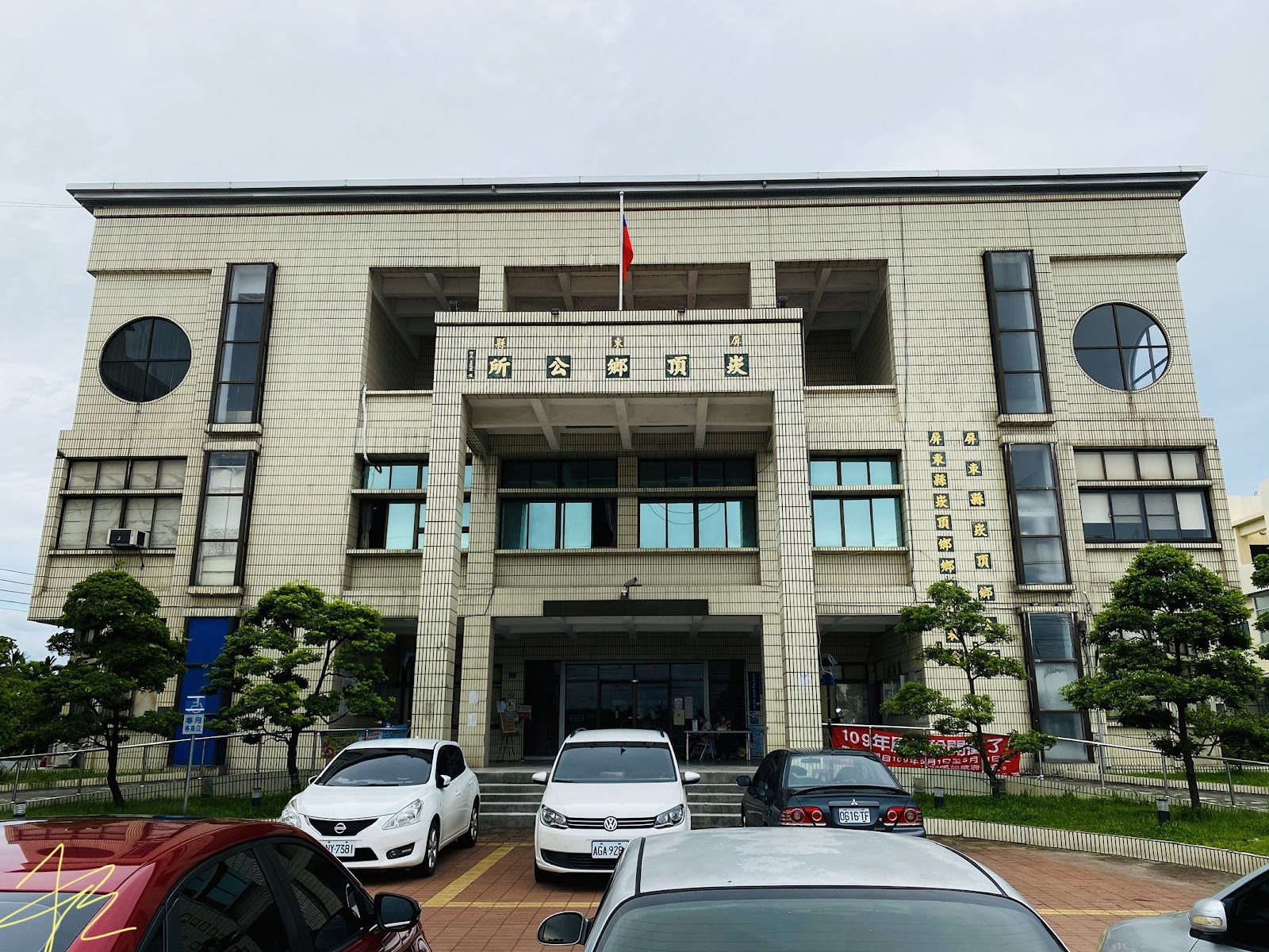 屏東縣崁頂鄉公所正面全景，白色與銀色轎車停滿前方廣場