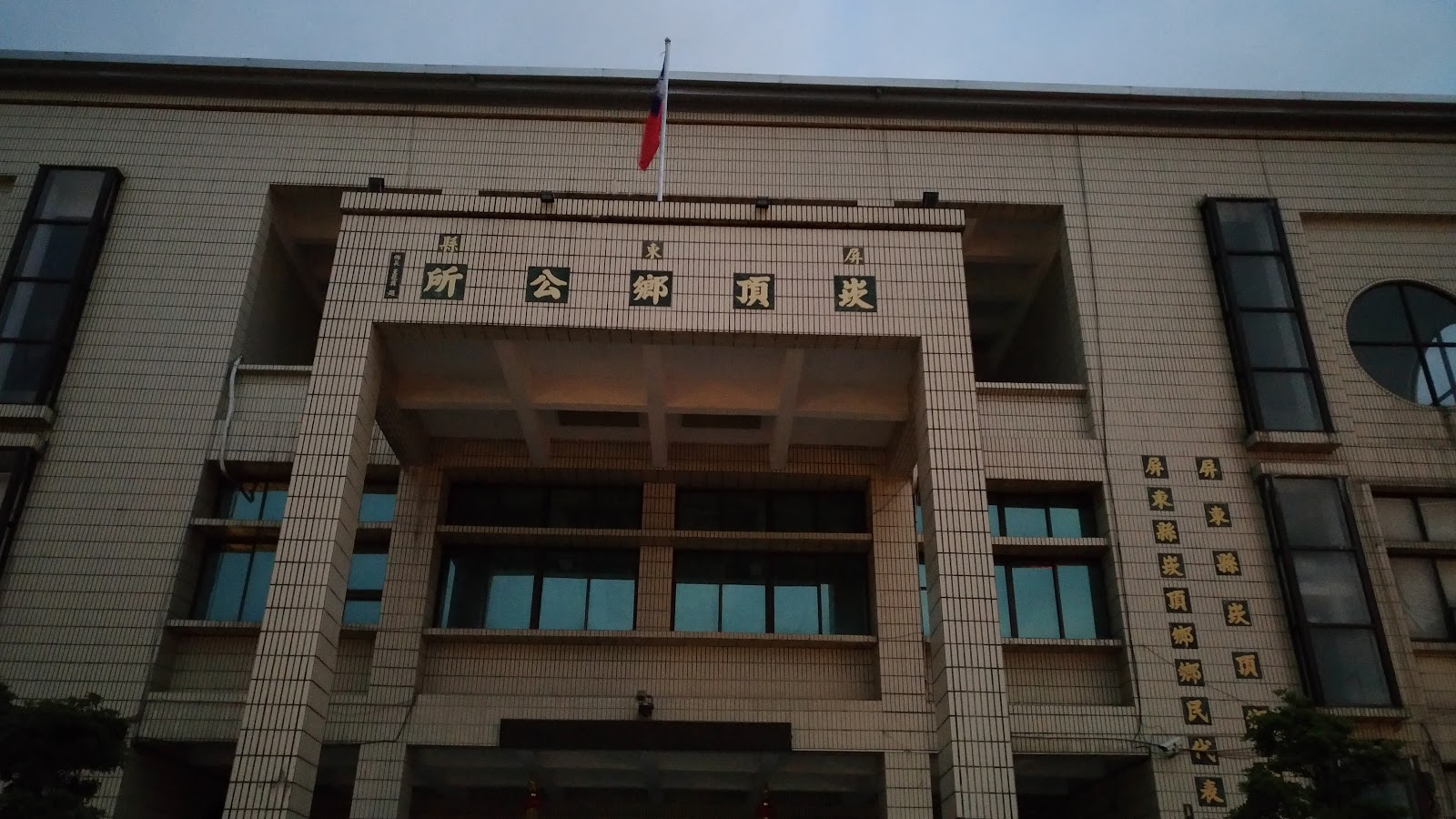 崁頂鄉公所牌樓仰角特寫,國旗與金色牌匾文字