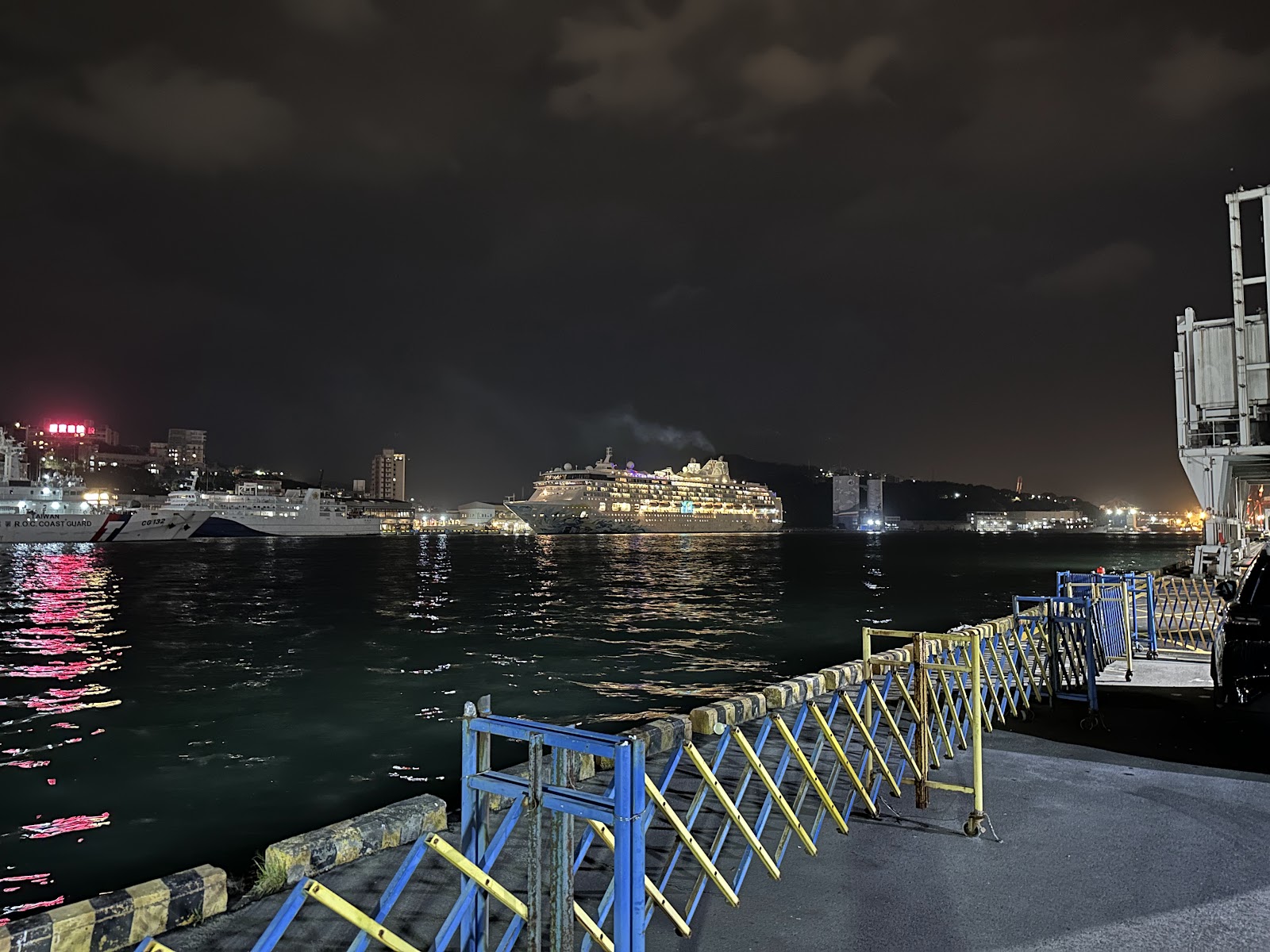 海洋廣場夜景遠眺郵輪與海巡艦艇停泊，棧道欄杆前景