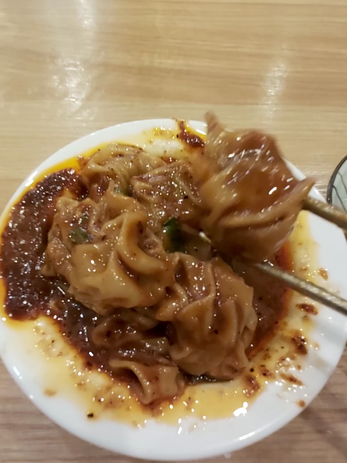 大碗牛肉麵紅油抄手特寫，筷子夾起沾滿辣油的抄手