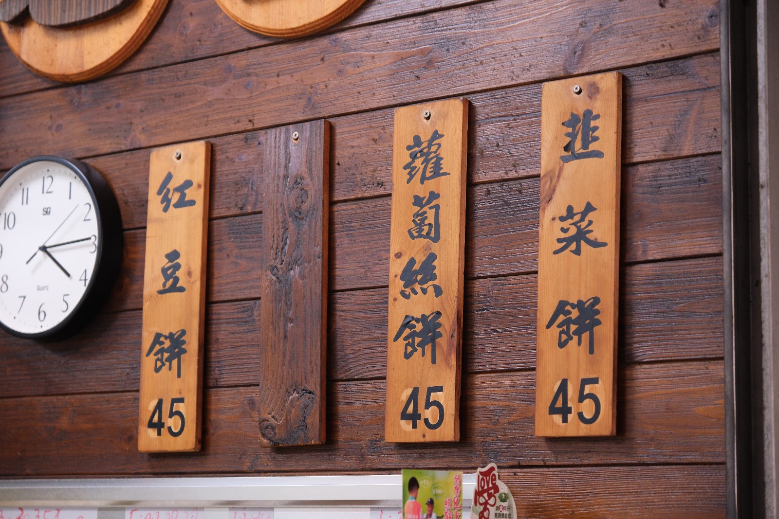 木牌手寫菜單「紅豆餅45／蘿蔔絲餅45／韭菜餅45」掛於木牆上搭配復古掛鐘