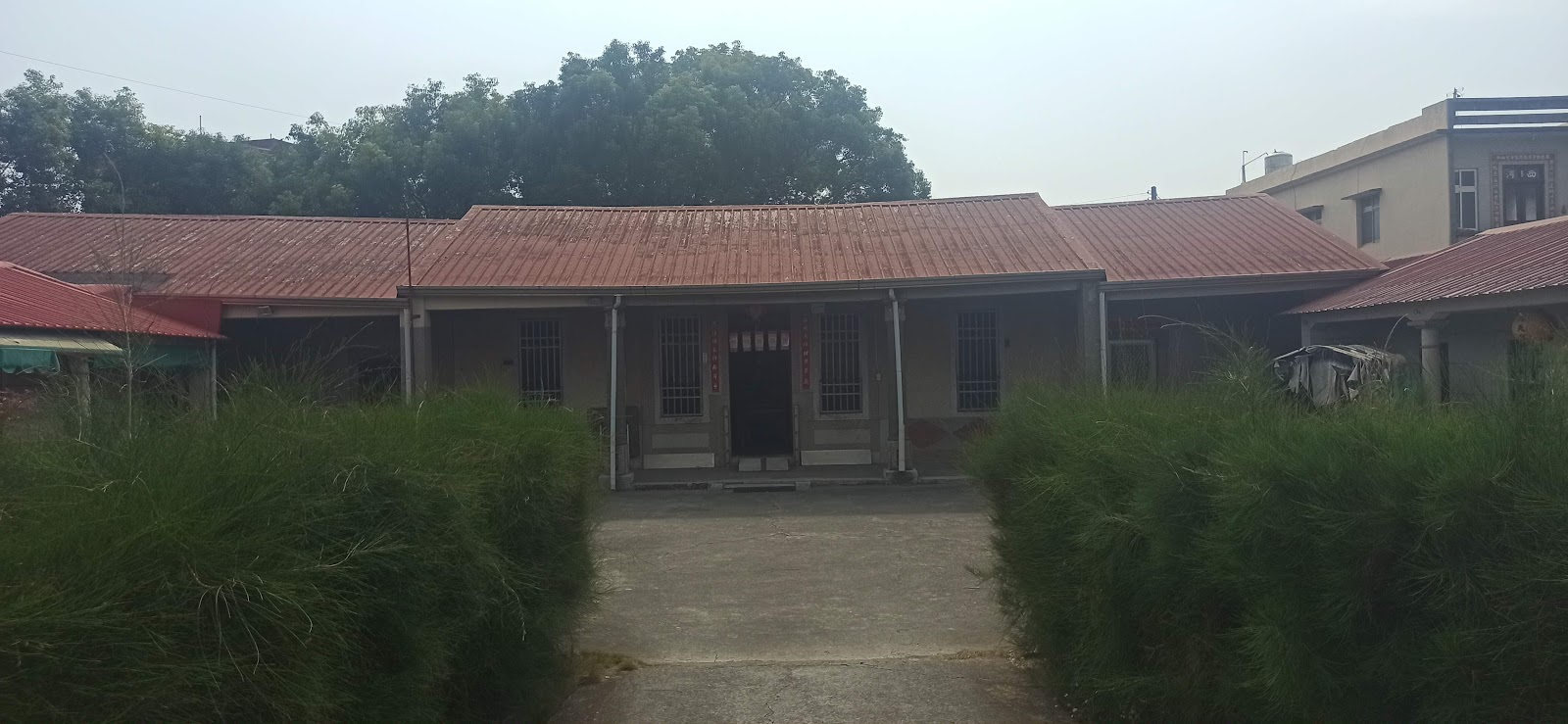 姚家古厝三合院正身全景，紅色鐵皮屋瓦與綠籬植栽