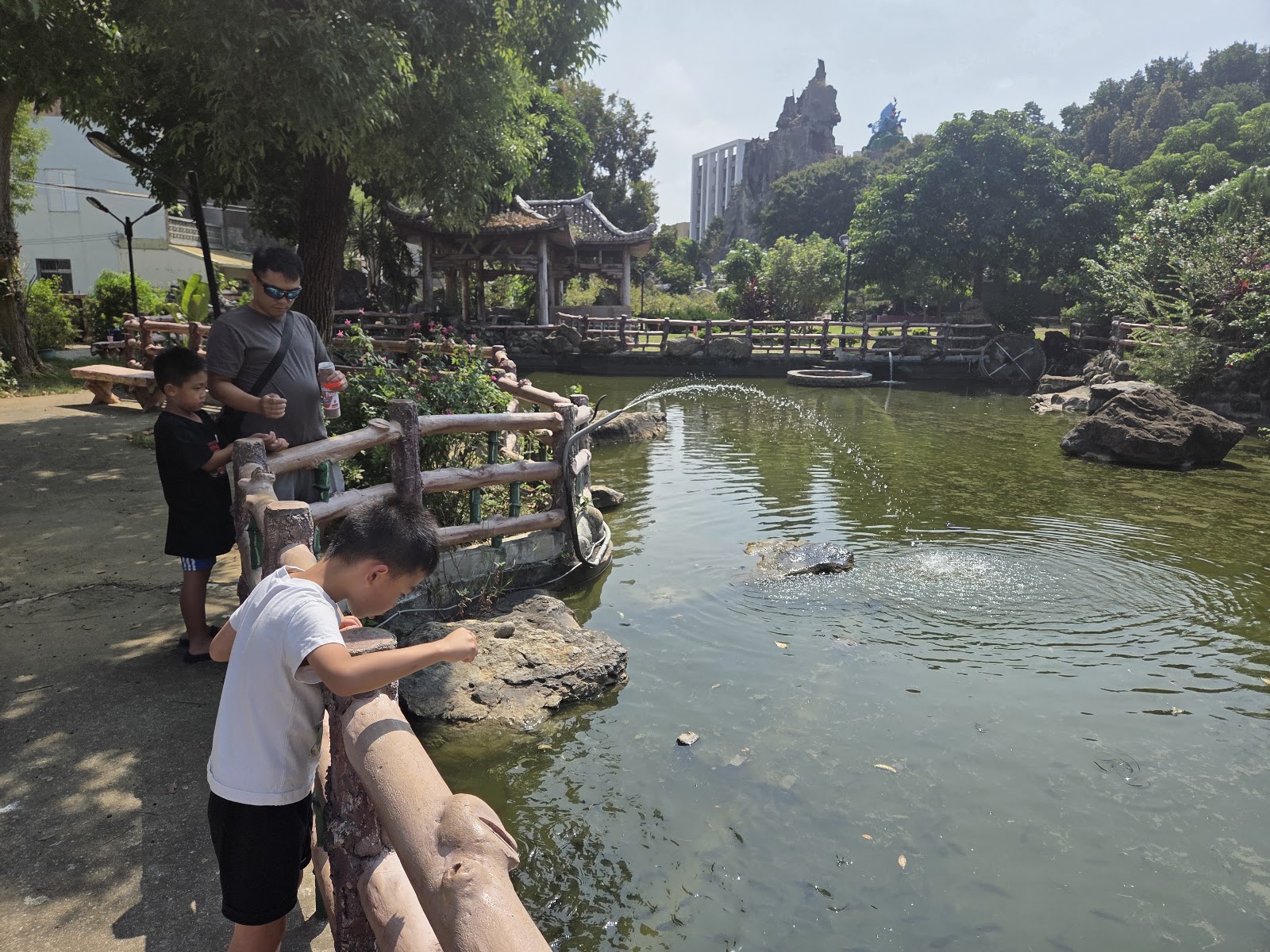 玉清公園景觀湖泊，親子在木造欄杆旁餵魚賞噴泉