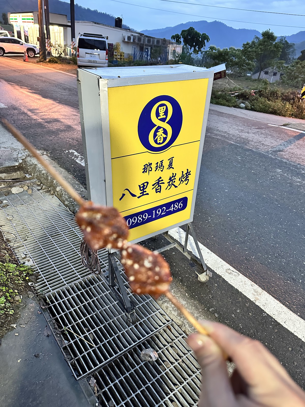 手持剛烤好的雞腿肉串,背景是八里香碳烤的招牌