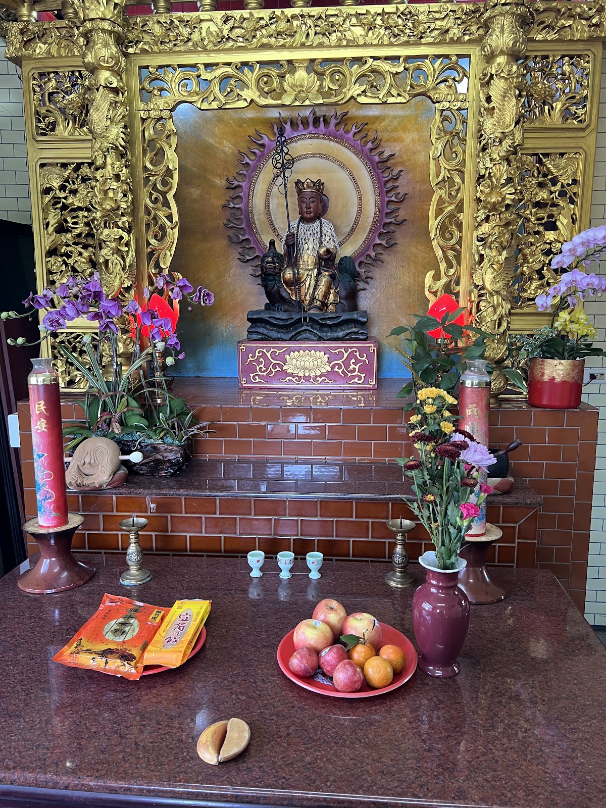 廟內神龕金色雕花神壇，供奉神像，前方供桌擺放水果、鮮花與香燭