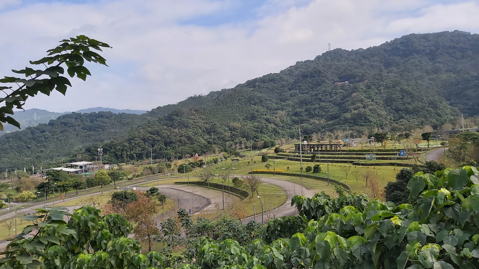 居高臨下俯瞰公園全景，環形車道、草坪、涼亭與遠方青山層疊