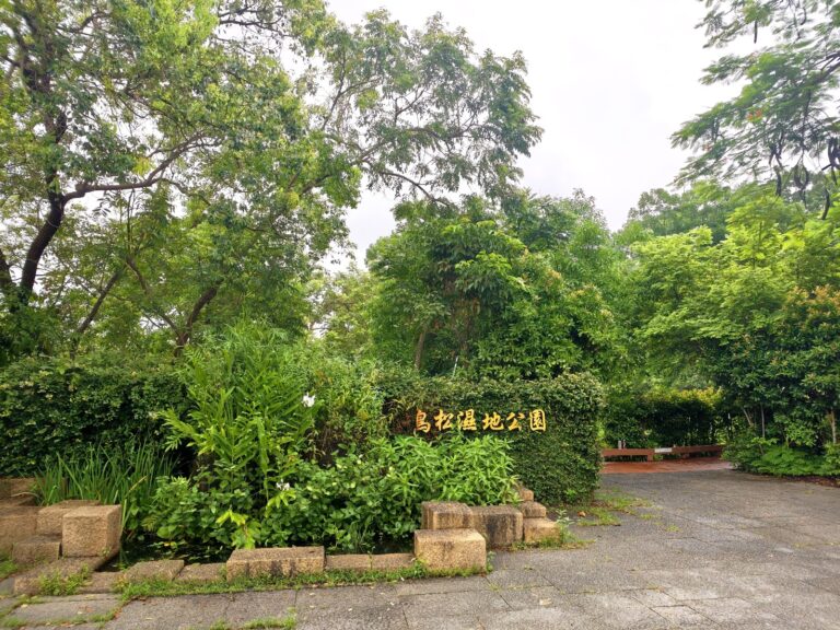鳥松濕地公園入口意象，木質招牌隱身綠蔭間