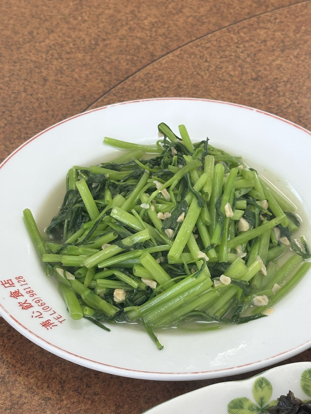 清心飲食店清炒地瓜葉青菜特寫,盤緣印有店家電話戳章