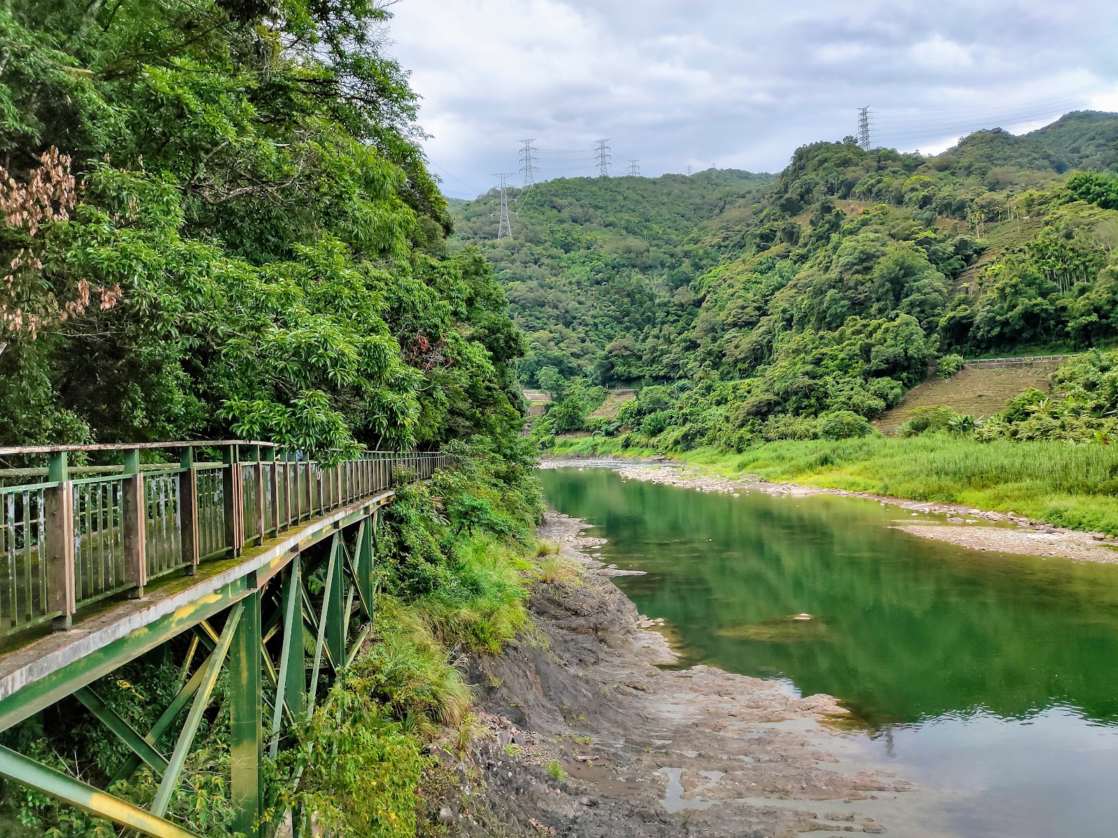 綠色高架觀魚步道沿著清澈碧綠溪水延伸，對岸山巒層疊
