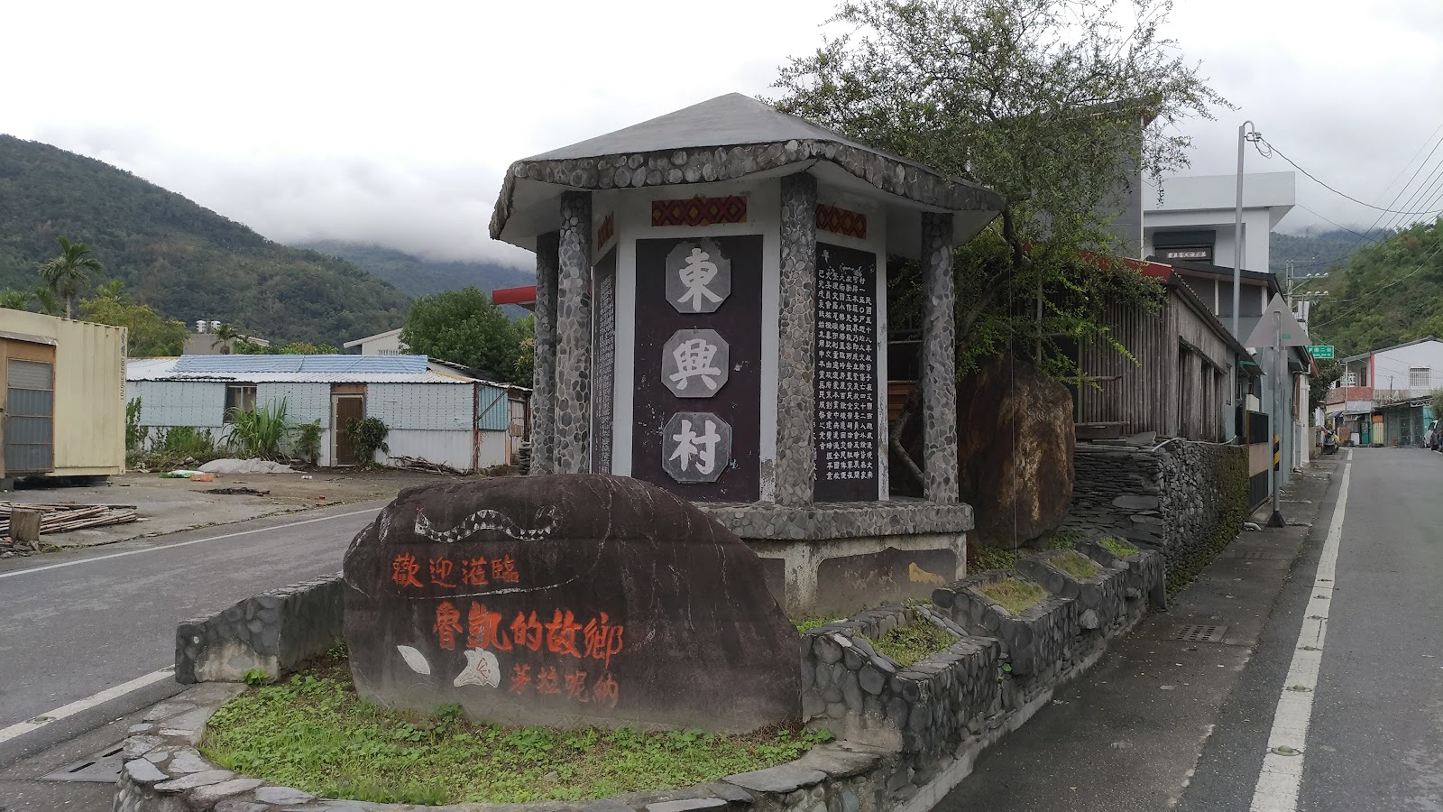 達魯瑪克紀念碑石雕人形碑體,紅字牌匾與棕梠樹背景