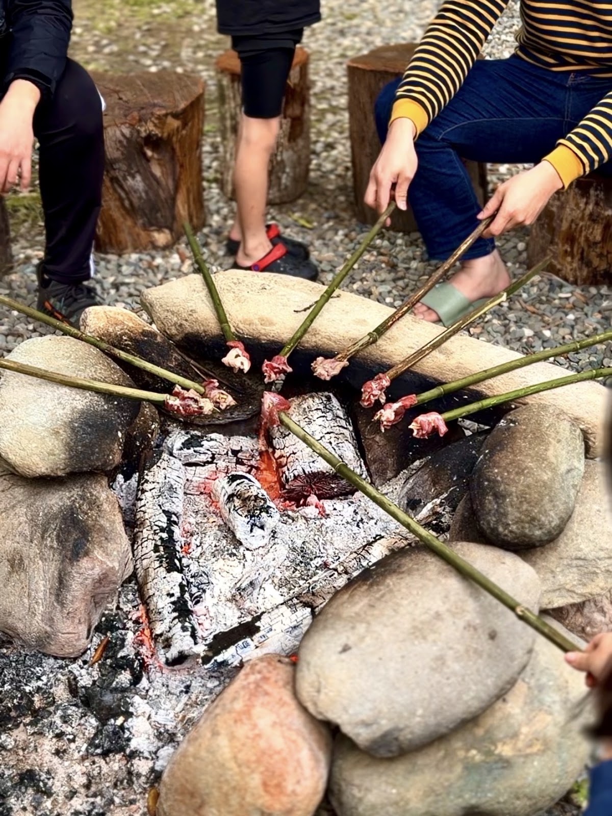 圍爐烤火體驗，木樁矮凳圍著碎石火堆，傳統料理正在炙烤