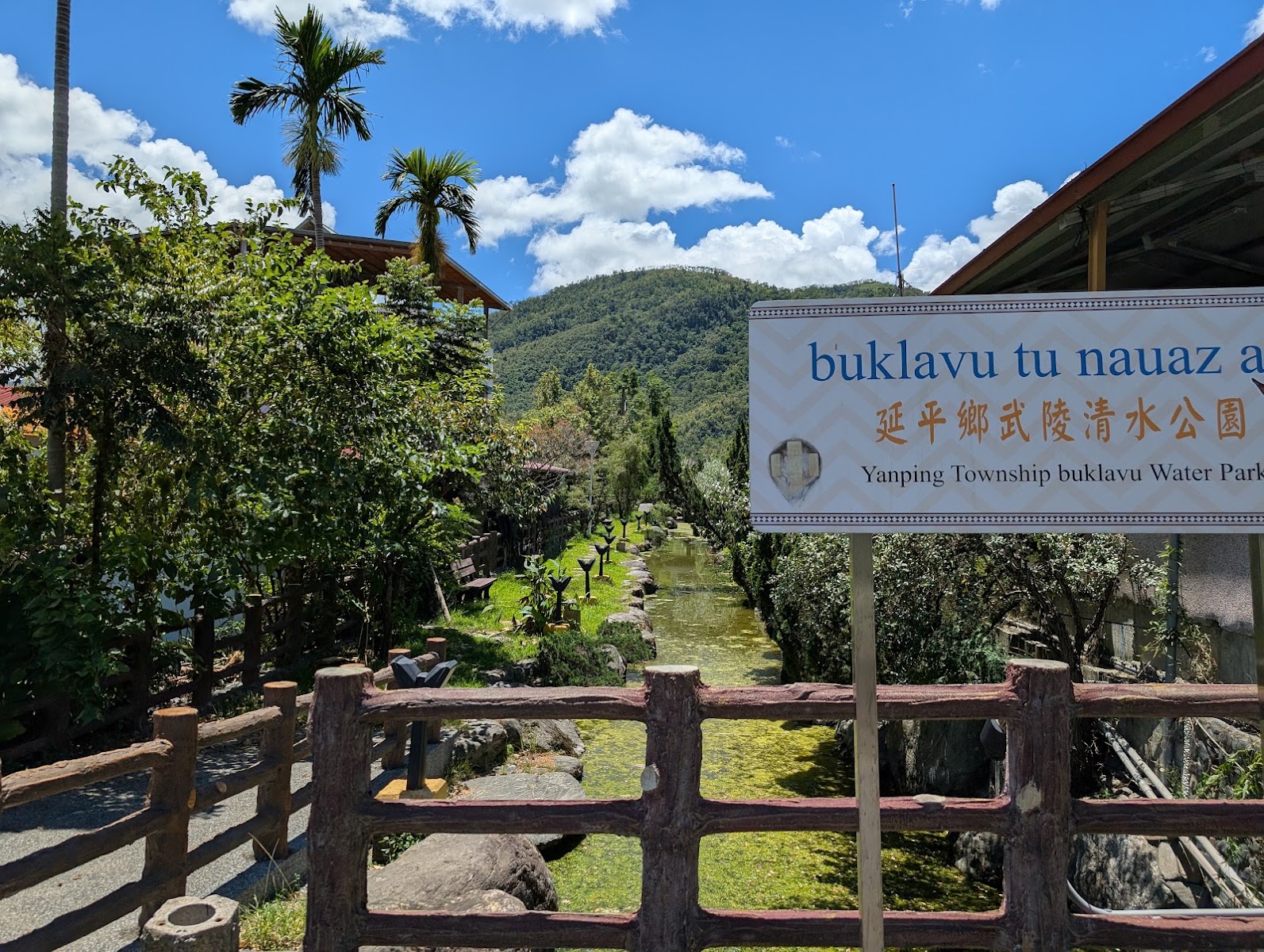 延平鄉武陵親水公園入口告示牌，木棧欄杆搭配藍天椰影