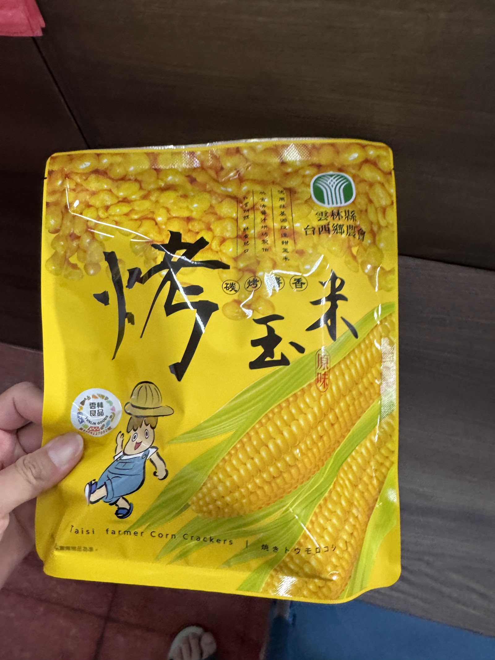 手持台西鄉農會烤玉米原味包裝袋特寫,包裝印有農會標誌與吉祥物圖案