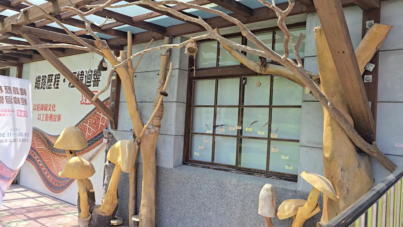 太魯閣族文創園區展覽館外觀，枯枝造型木雕裝置藝術與香菇造型木雕，窗邊貼有特展海報