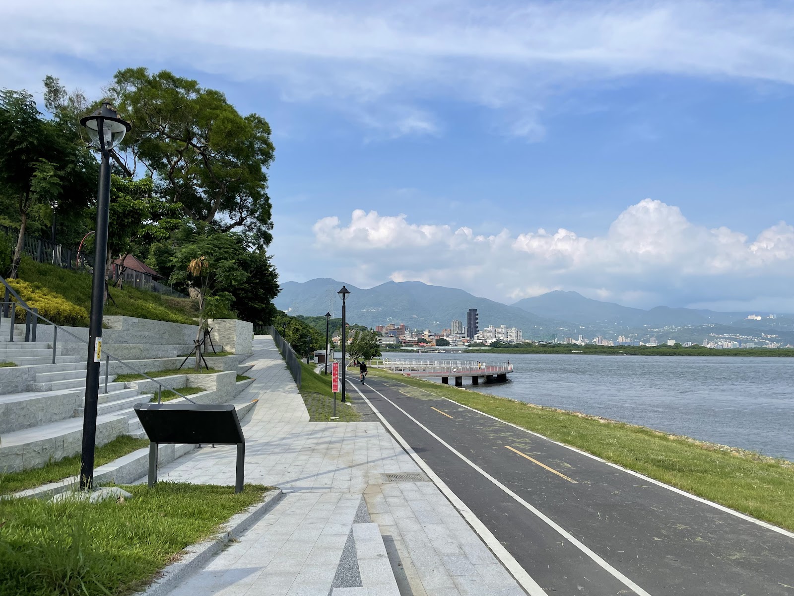 五股獅子頭山水匯集廣場河濱階梯座位看台與自行車道,遠方觀音山與淡水河對岸城市天際線