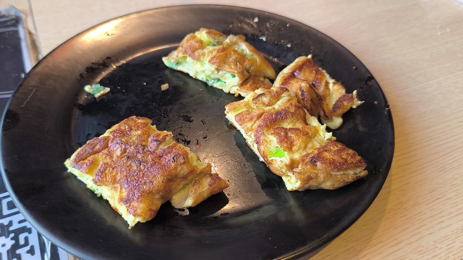 黑色餐盤上的煎蛋餅料理特寫，金黃焦邊夾著蔥花