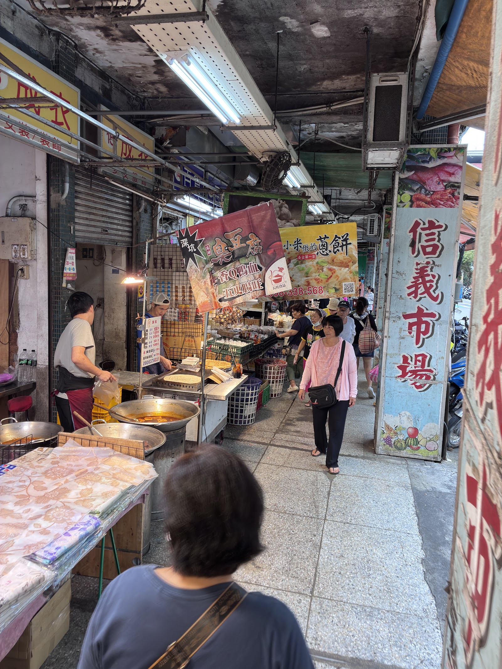 信義市場內部巷道,攤商招牌林立,信義市場直式招牌清楚可見