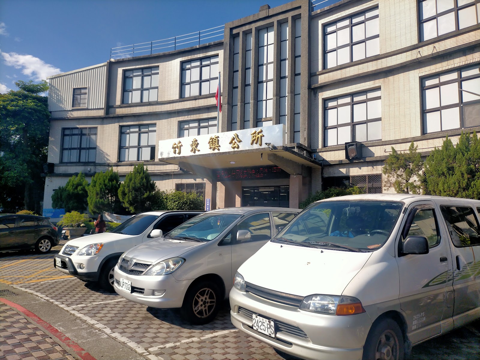 竹東鎮公所建物正面全景,晴朗藍天下停滿公務車輛